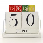 End of Financial Year Savings Concept with end of financial year building blocks and wood calendar on white wood table.