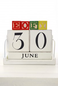 End of Financial Year Savings Concept with end of financial year building blocks and wood calendar on white wood table.